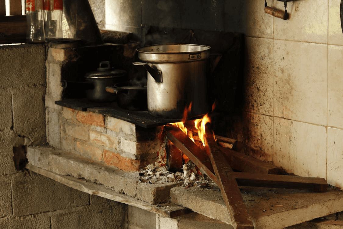 large metal pan on hob on bricks with firewood next to it