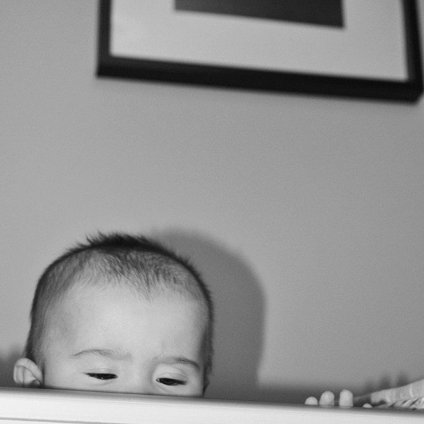 black and white shot of baby peeping over the top of cot