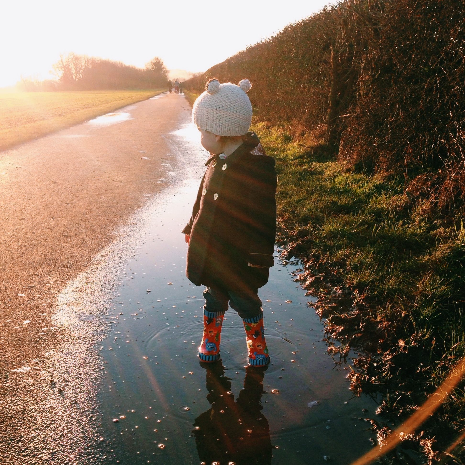 young child in evening sunlight standing in puddle