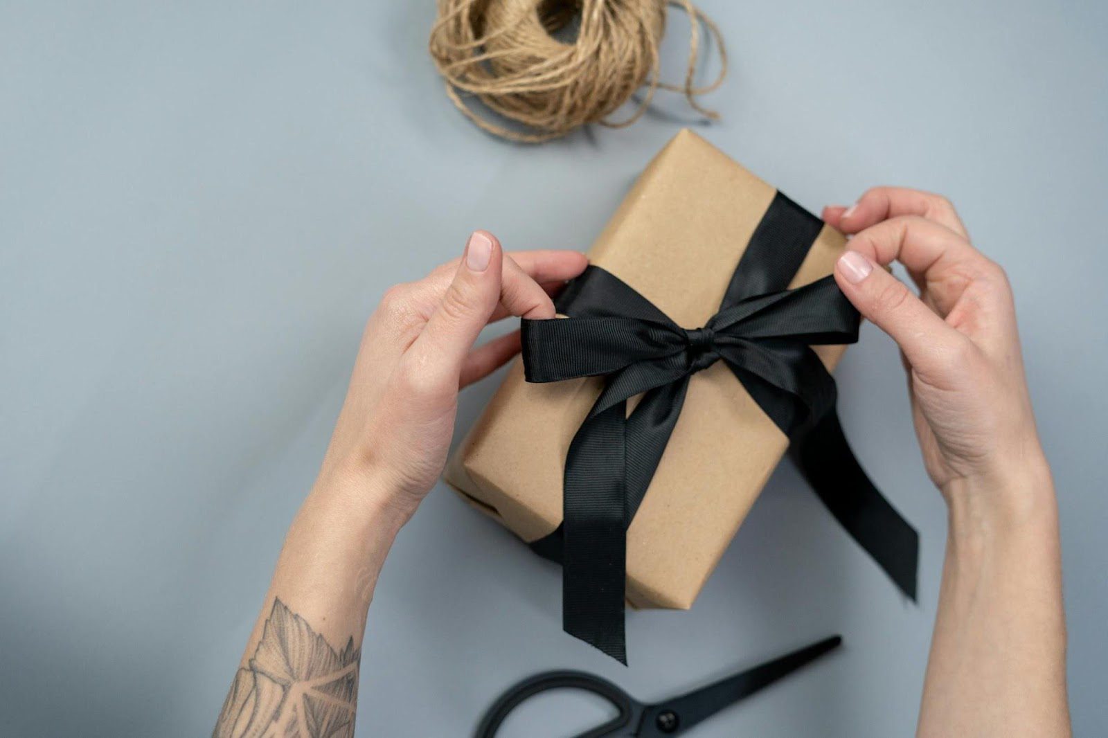 hands tying black bow on gift wrapped in brown paper