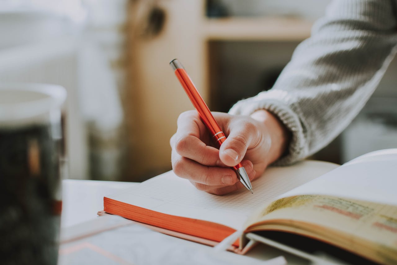 hand holding orange pen writing in notebook