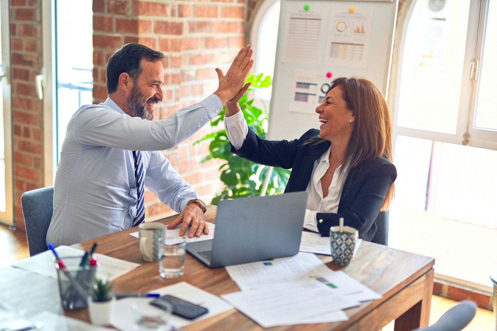 man and woman high-fiving at desk with laptop and paperwork