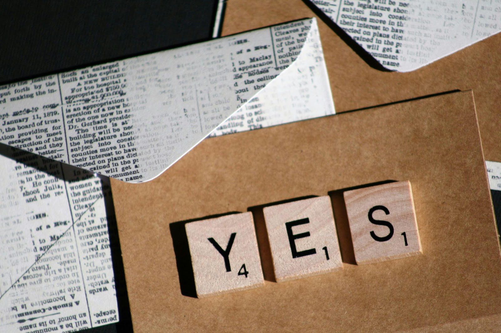 brown scrabble letters spelling out yes on brown paper with envelope in background