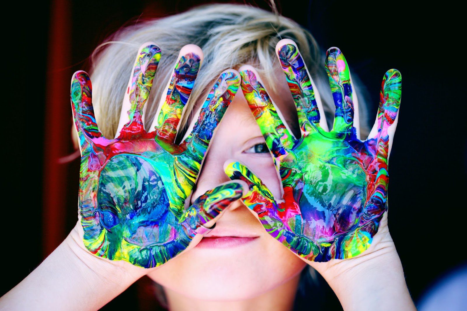 child with painted hands up in front of face