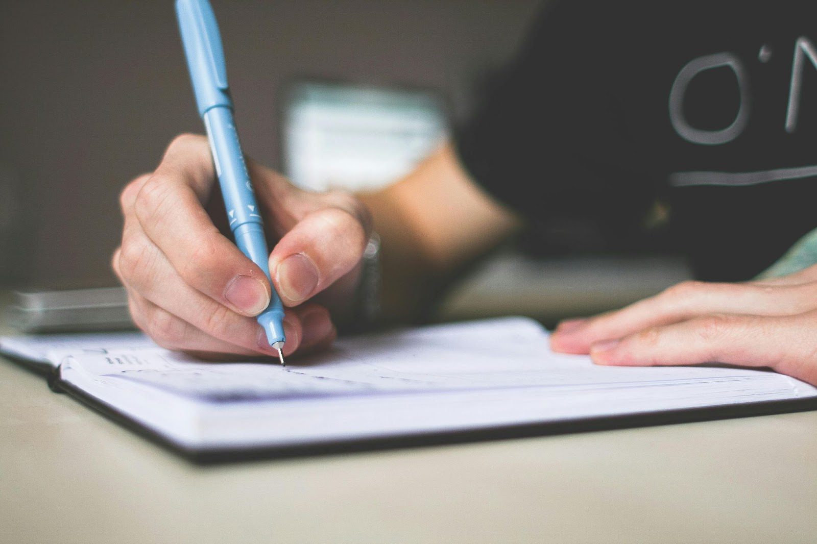 hands up close writing with a blue pen in a notebook