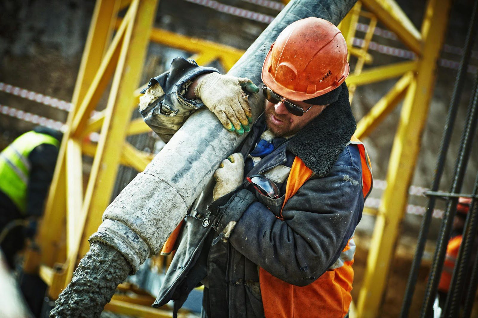 builder in hard hat on conctruction site, carrying large concrete post