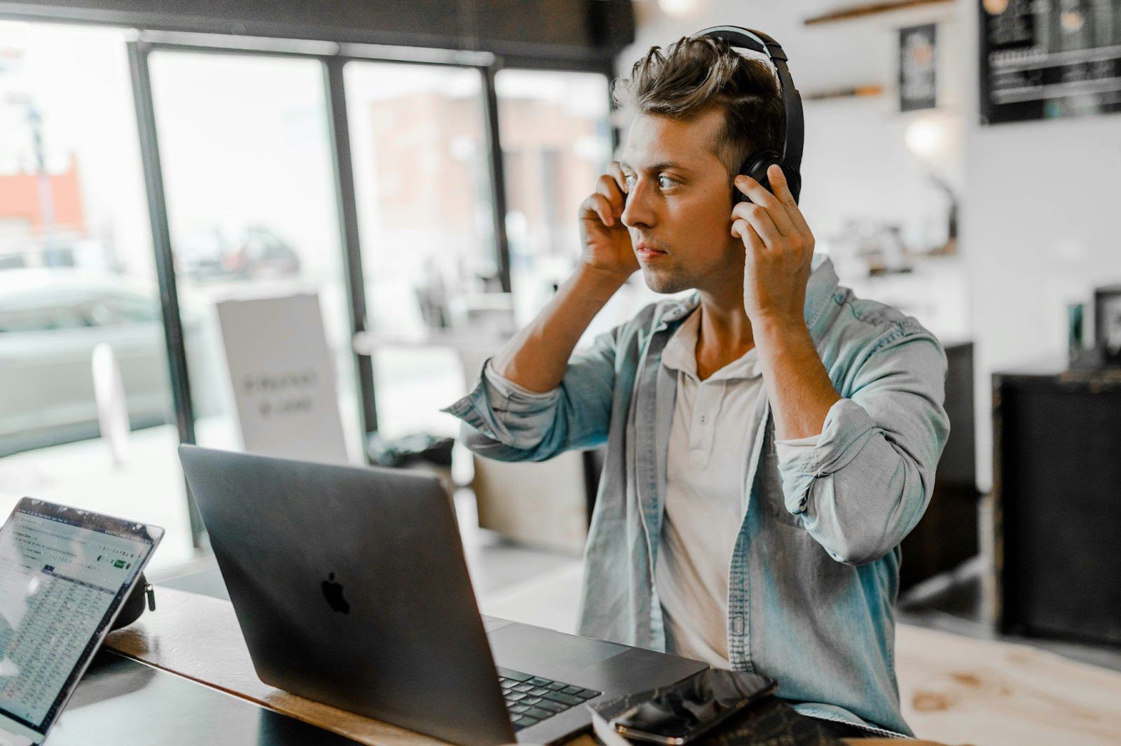 man stood at desk with laptop open, wearing headphones