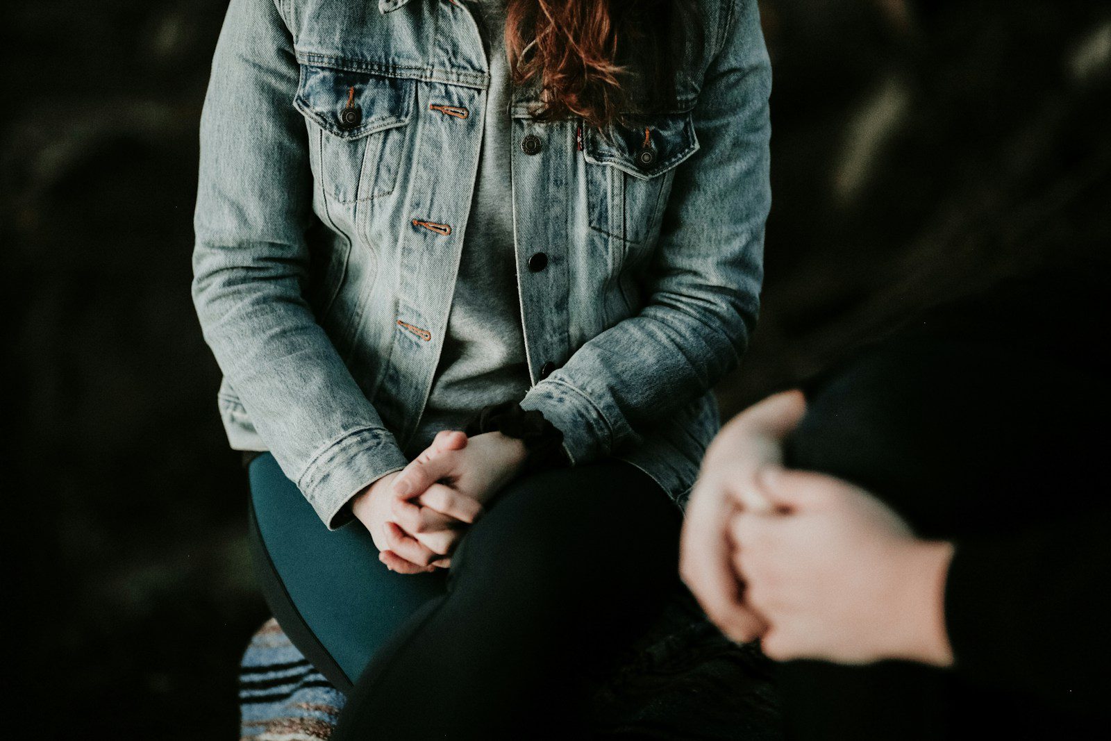 woman wearing jacket sitting down next to someone else