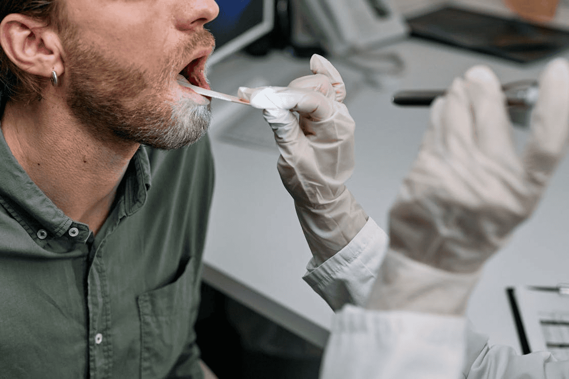 dentist wearing white latex glove looking into mouth of male patient