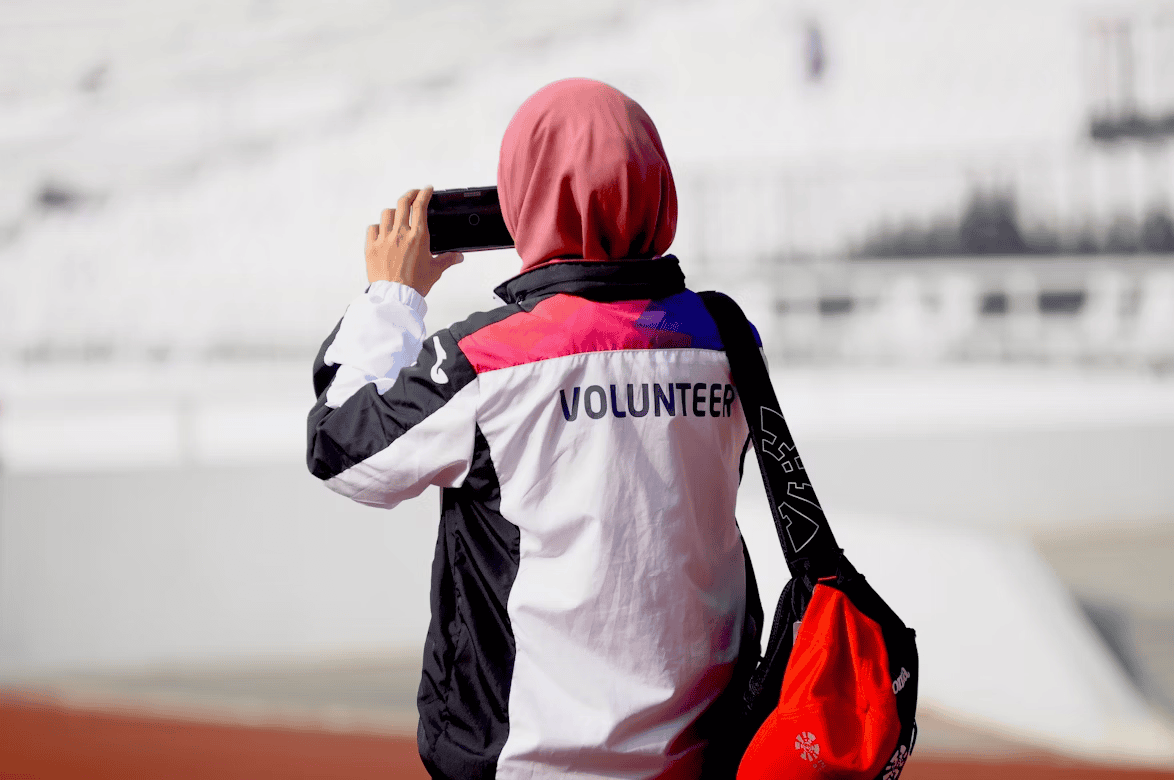 woman wearing headscarf and a volunteer jacket holding phone up to take a photo