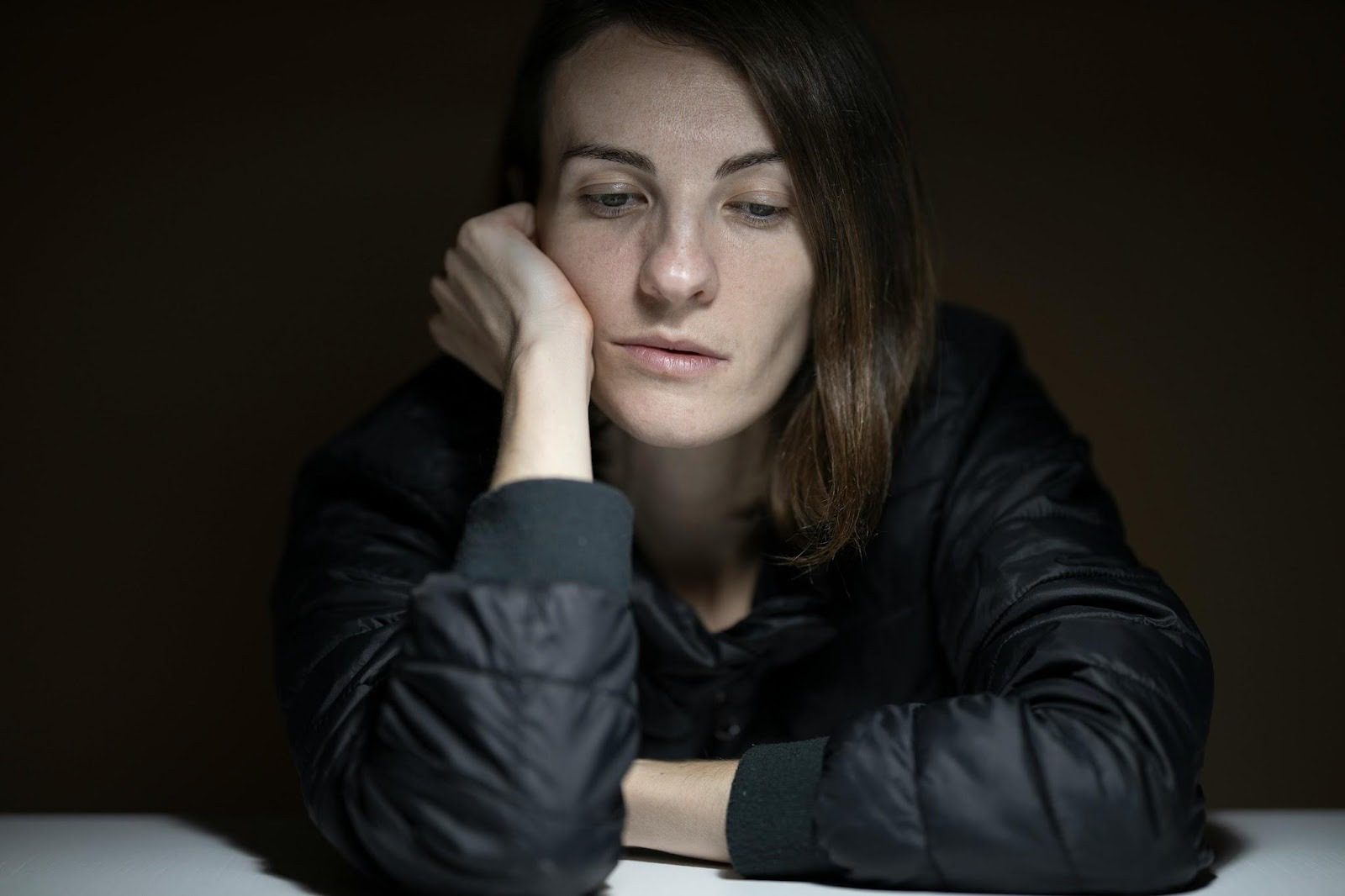 woman in black coat, sitting at table when head in hands, looking sad