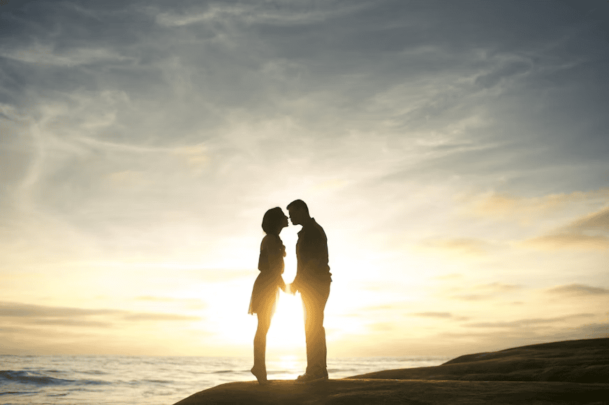 couple standing on hill in sunlight, facing each other, holding hands and kissing