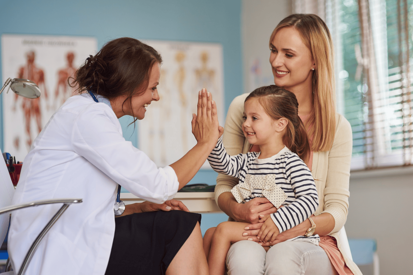 doctor in white coat high fiving a young girl ositting on mothers knee