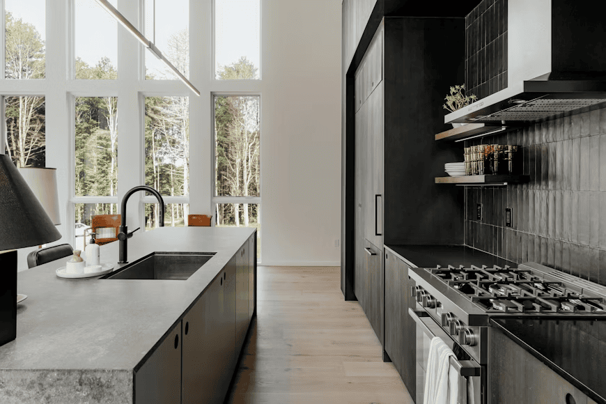 long, modern kitchen with dark cupboards and big windows