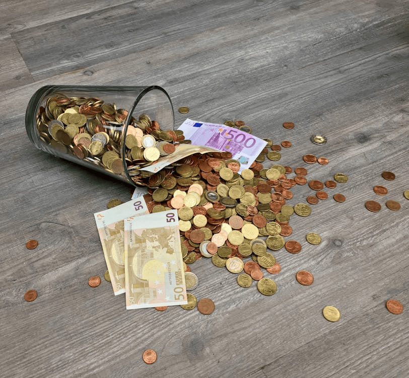 notes and cash money spilling out of glass onto surface