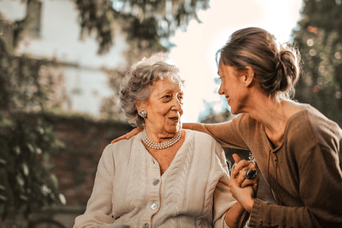 two women - one older and one younger - sitting together, holding hands and smiling