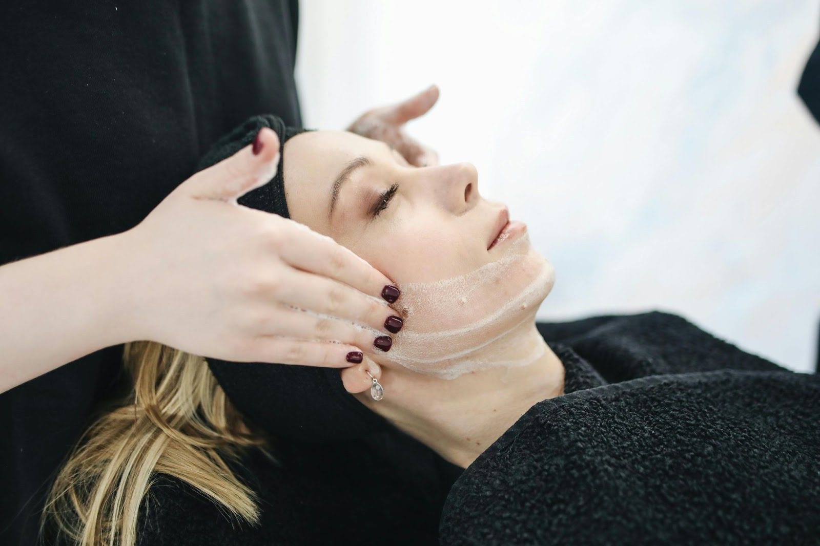person lying with their eyes closed having their face massaged