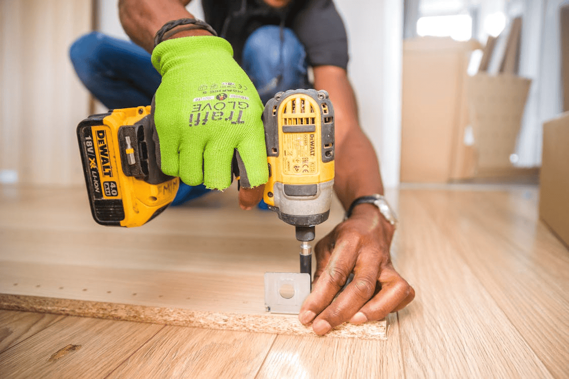 man wearing gleen glove, drilling into wood on floor