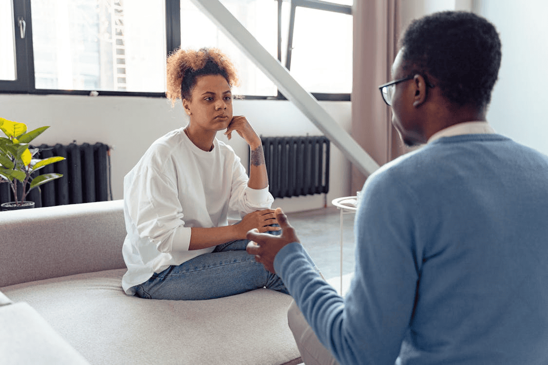 a woman sitting on a sofa opposite a man who is talking to her