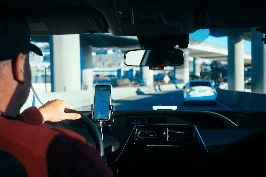 person driving car on road with phone in holder and open on maps