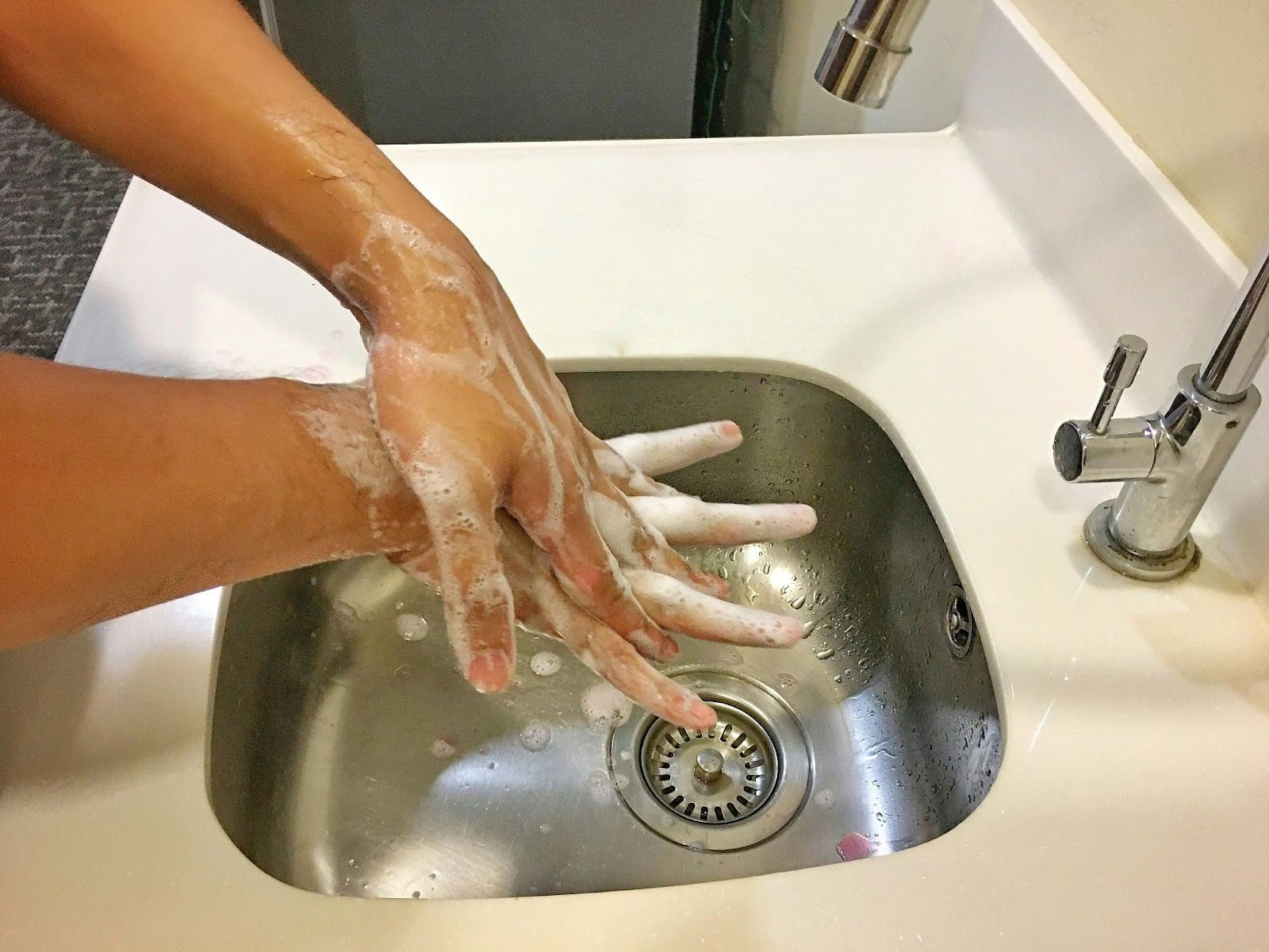 person with soapy hands washing them at sink