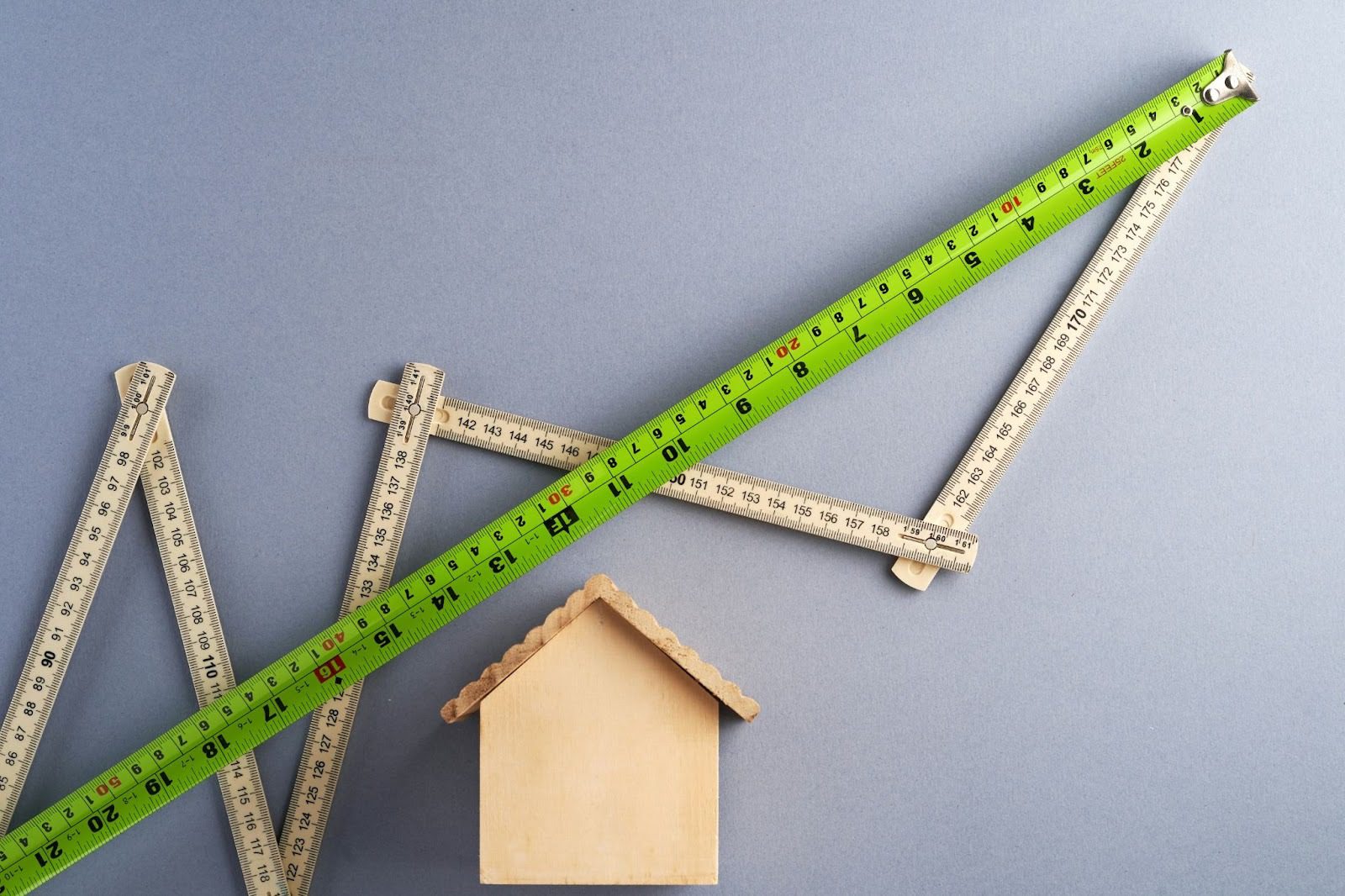 green tape measure against wooden bending ruler and wooden house block