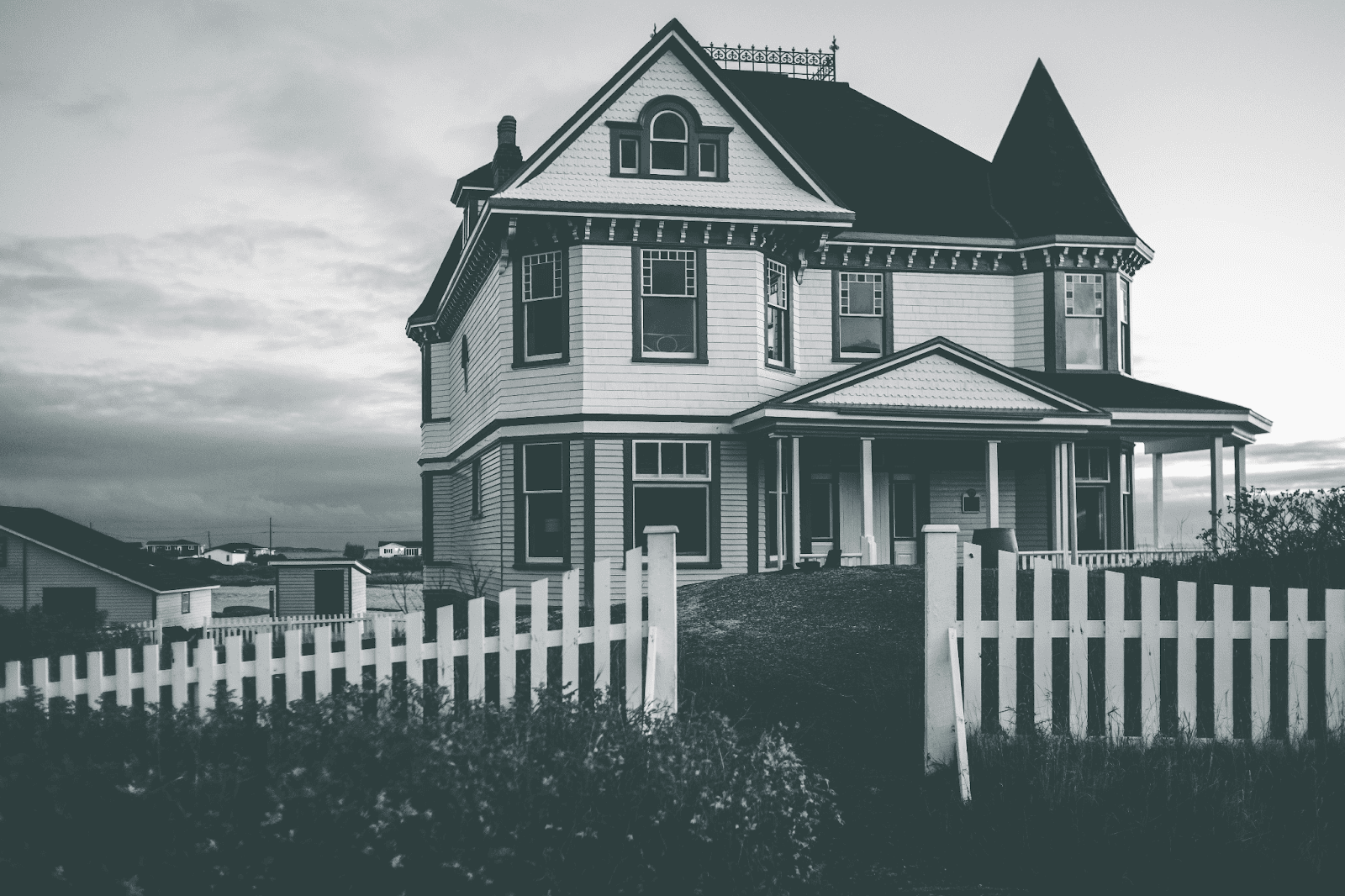 black and white photo of large house with white fence around it