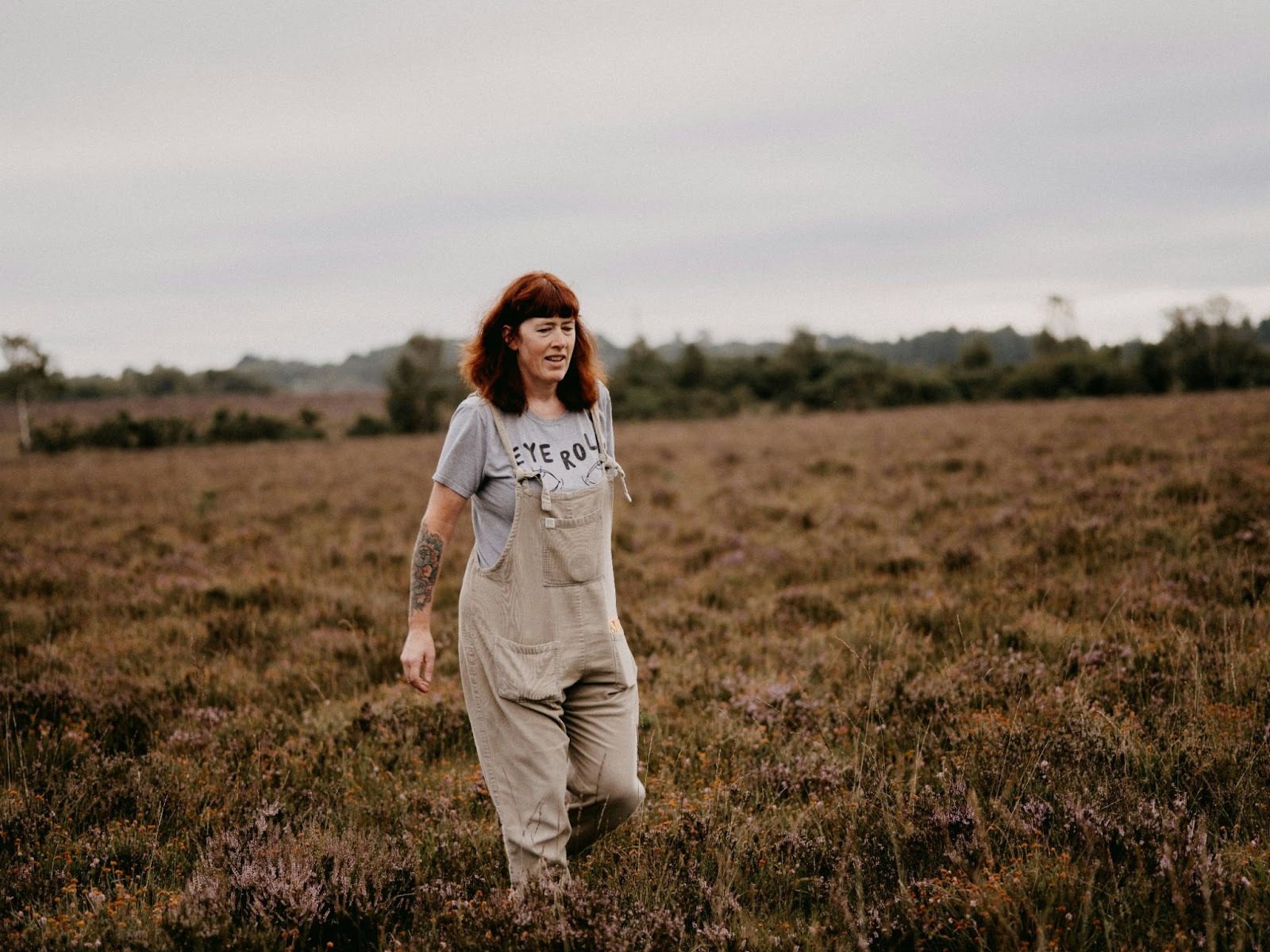 woman wearing dungarees walking through brown grassy field