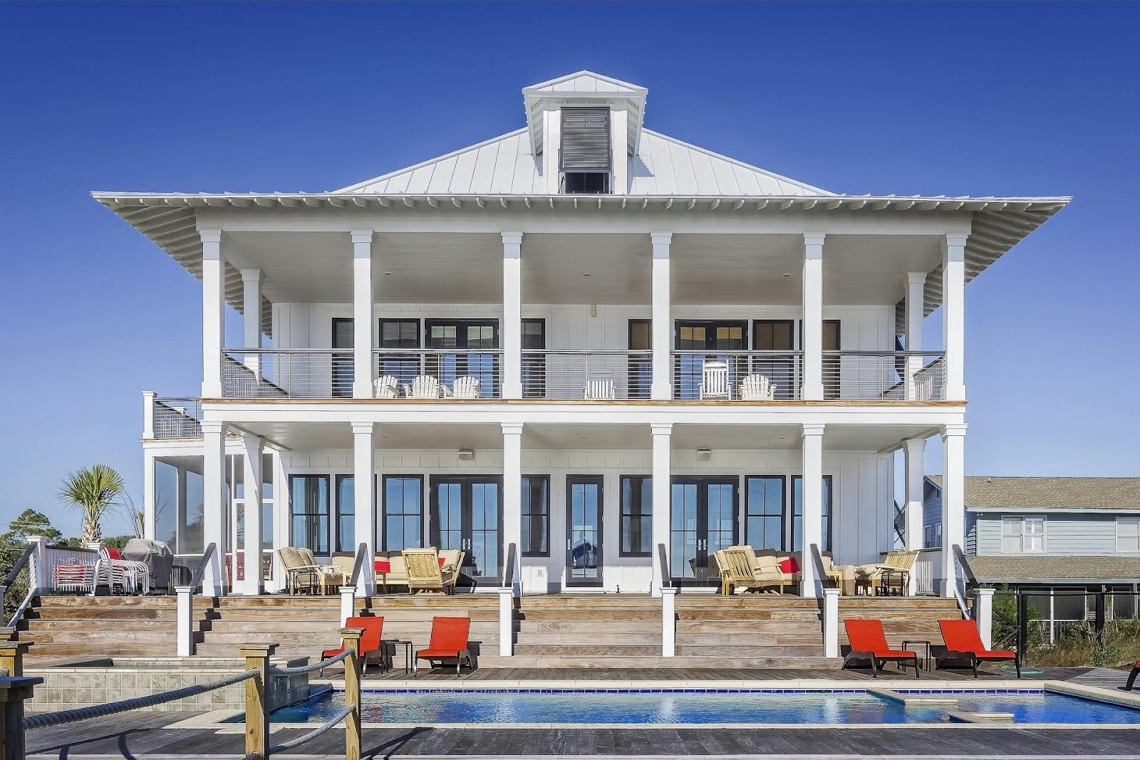 big white house with columns and red sunbeds in front of it, next to pool