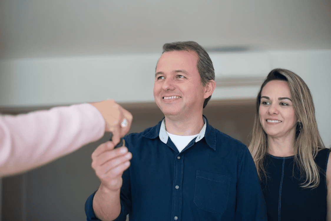 woman standing next to man in house, who is taking a key from another person's hand