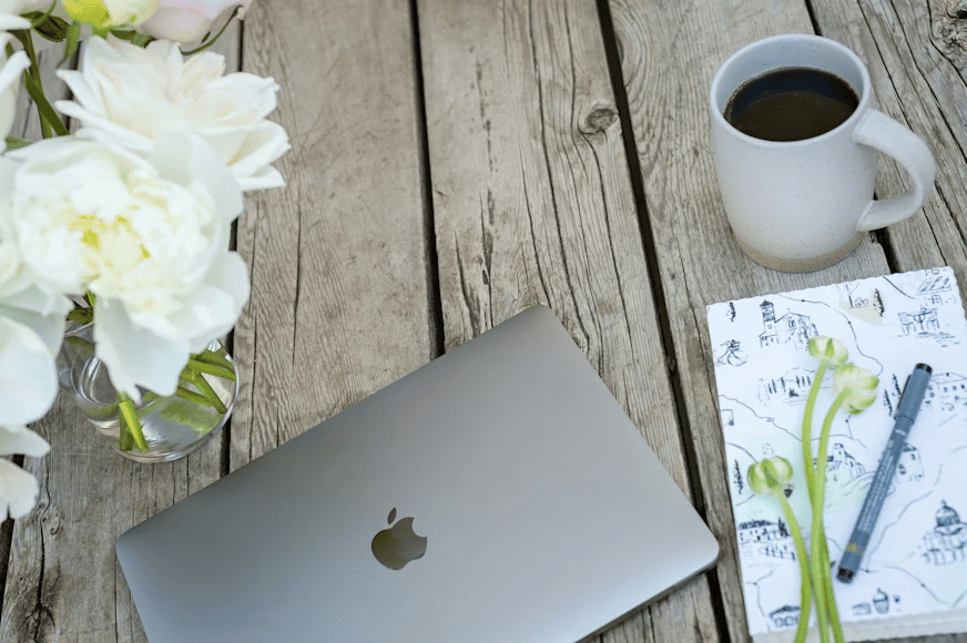 laptop on wooden table next to flowers