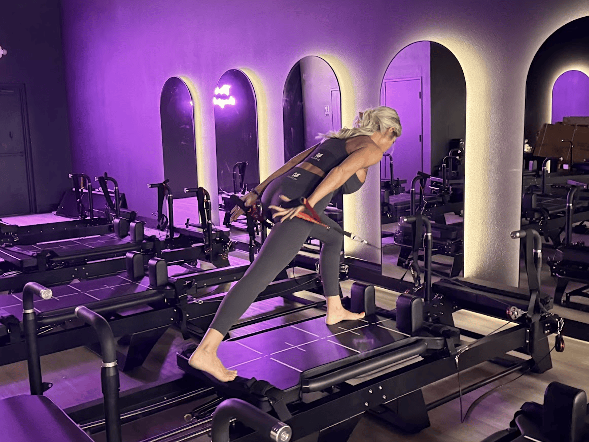 woman on reformer pilates machine in studio with purple lights