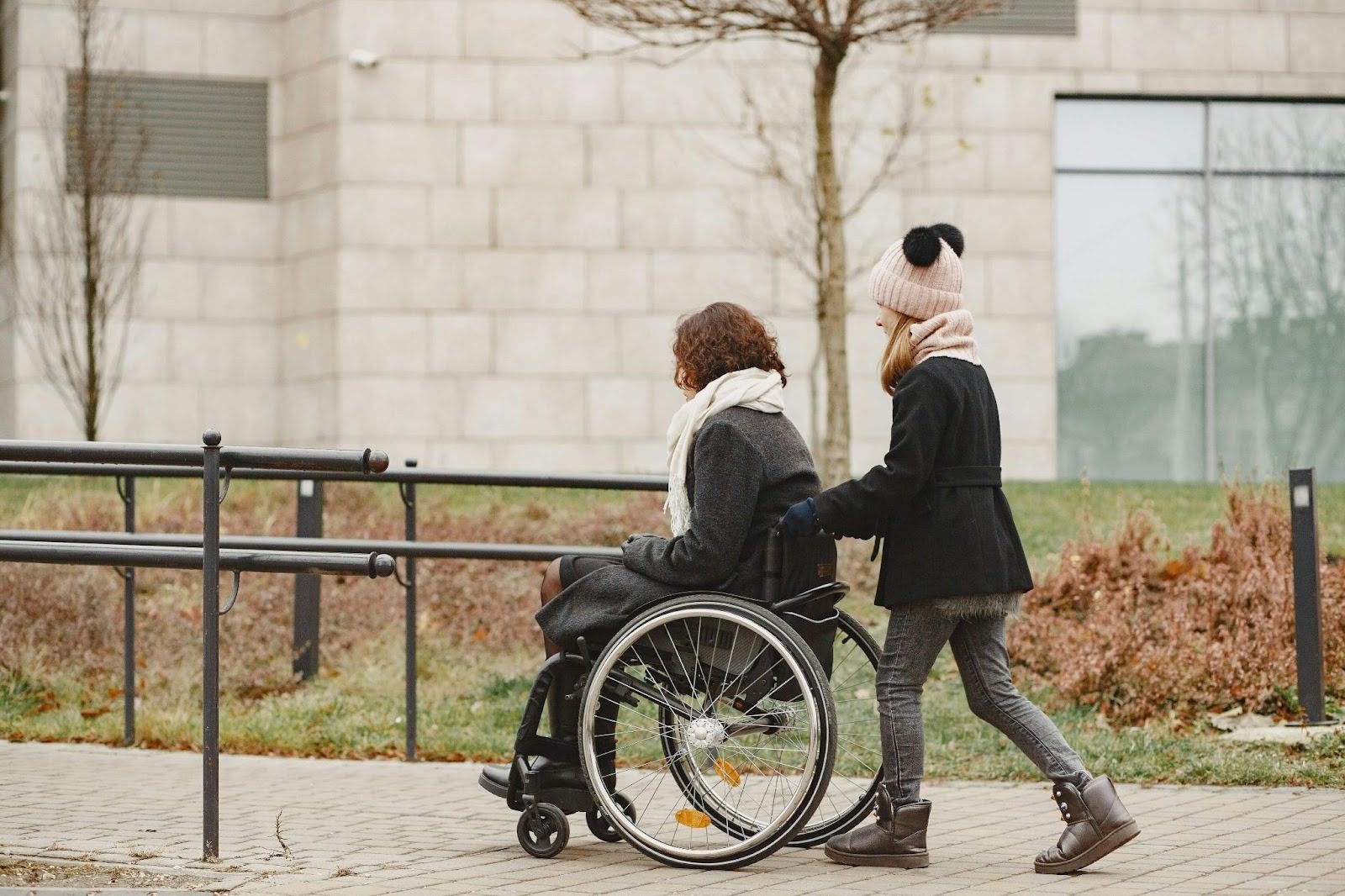 woman pushing another woman in a wheelchair outside
