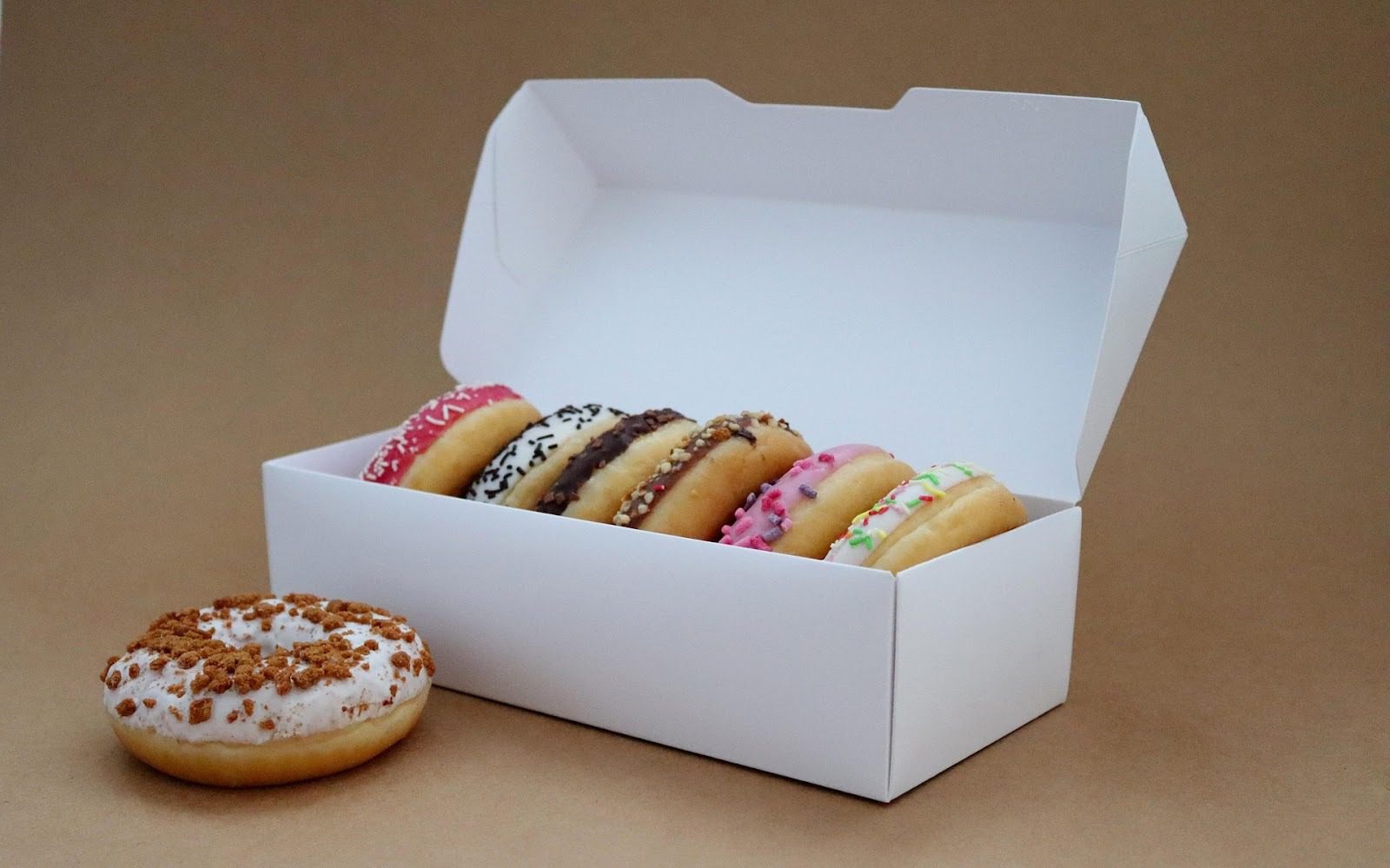 iced doughnuts in a white box with one sitting next to it