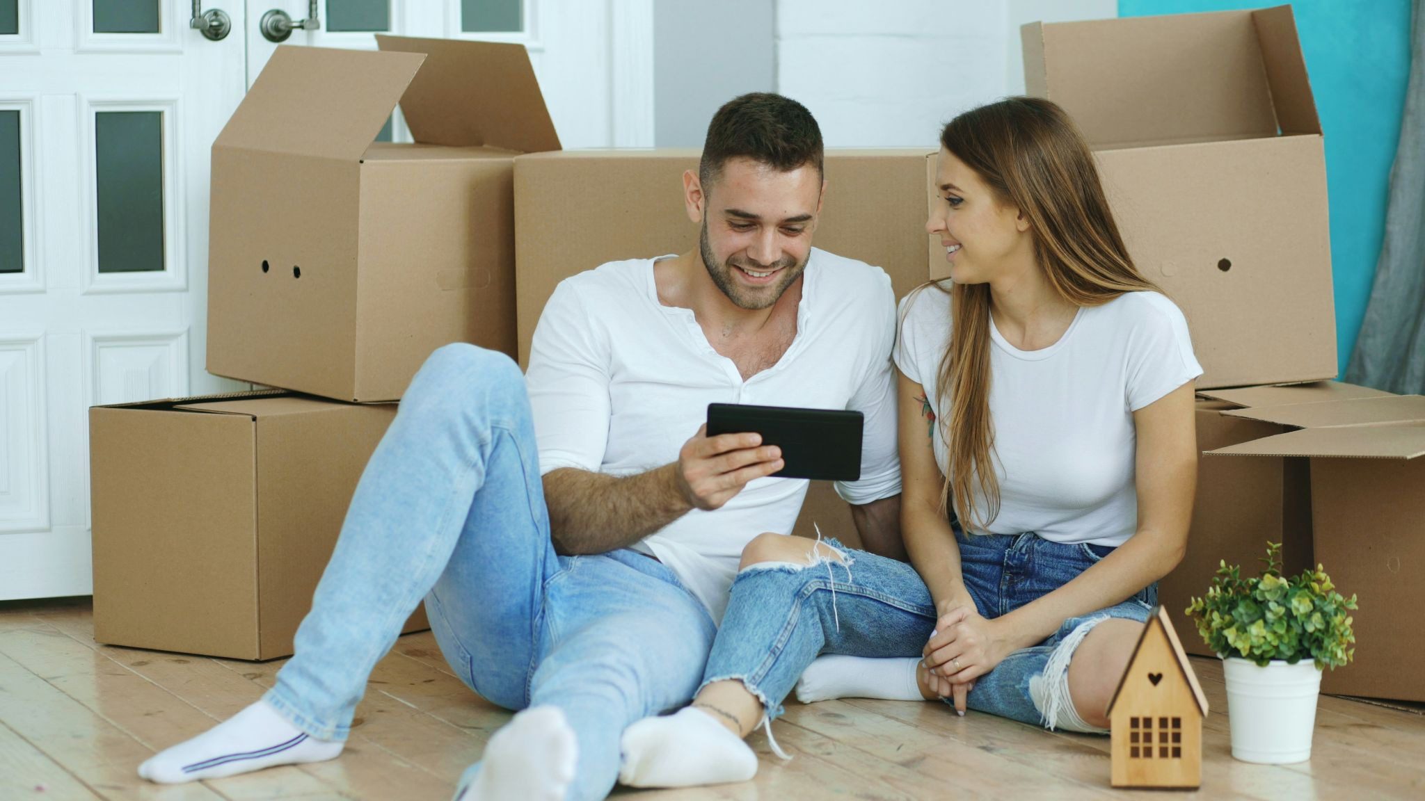 man and woman sitting on floor looking at phone, with boxes piled behind them