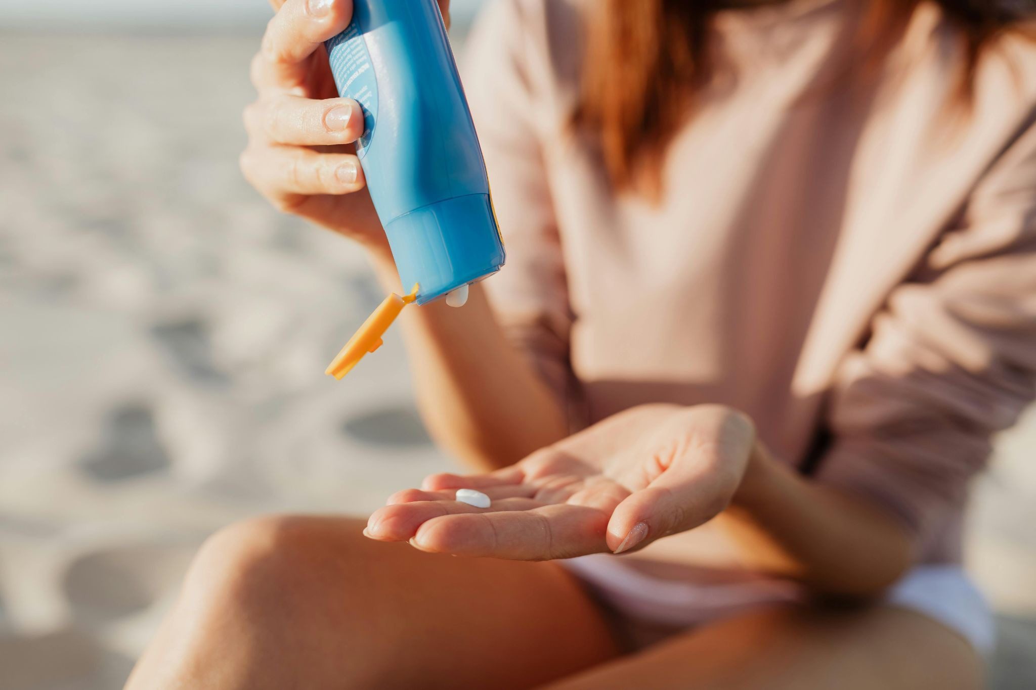 woman on beach squeezing blue bottle of sun cream into hand