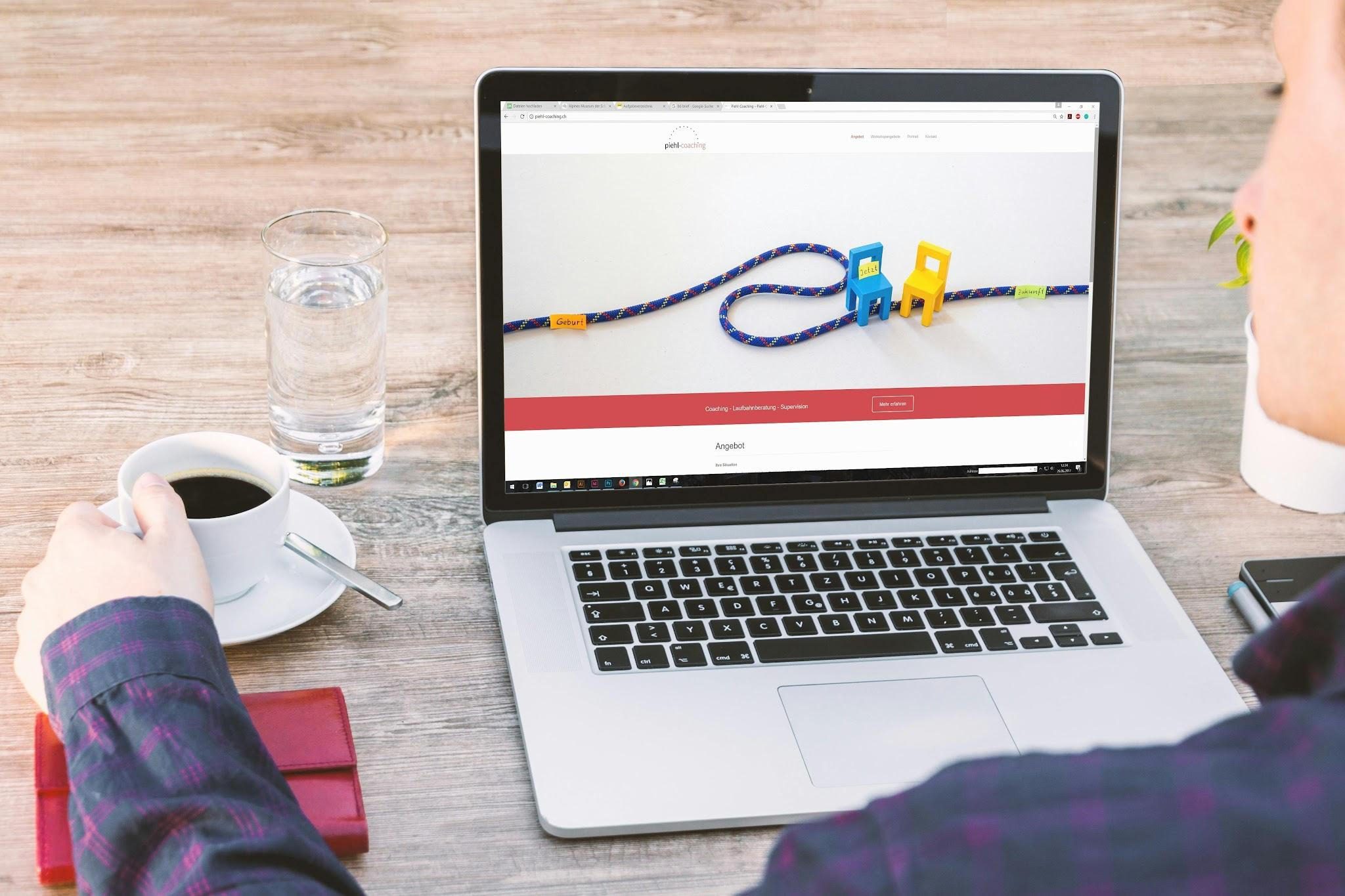person sitting at table in front of open laptop with cup of coffee and water