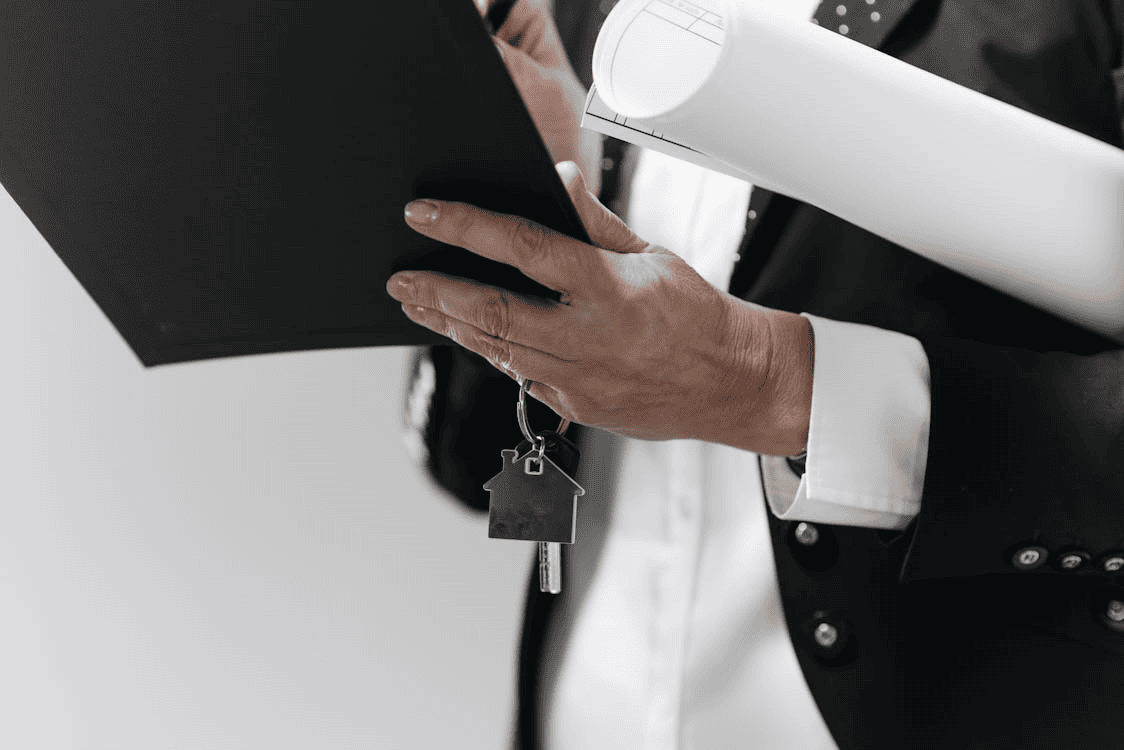 person holding black folder and keys with house-shaped key ring on them