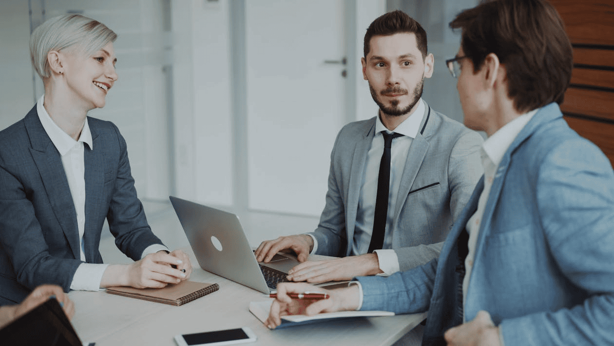 3 people in business meeting, sitting at desk with laptops