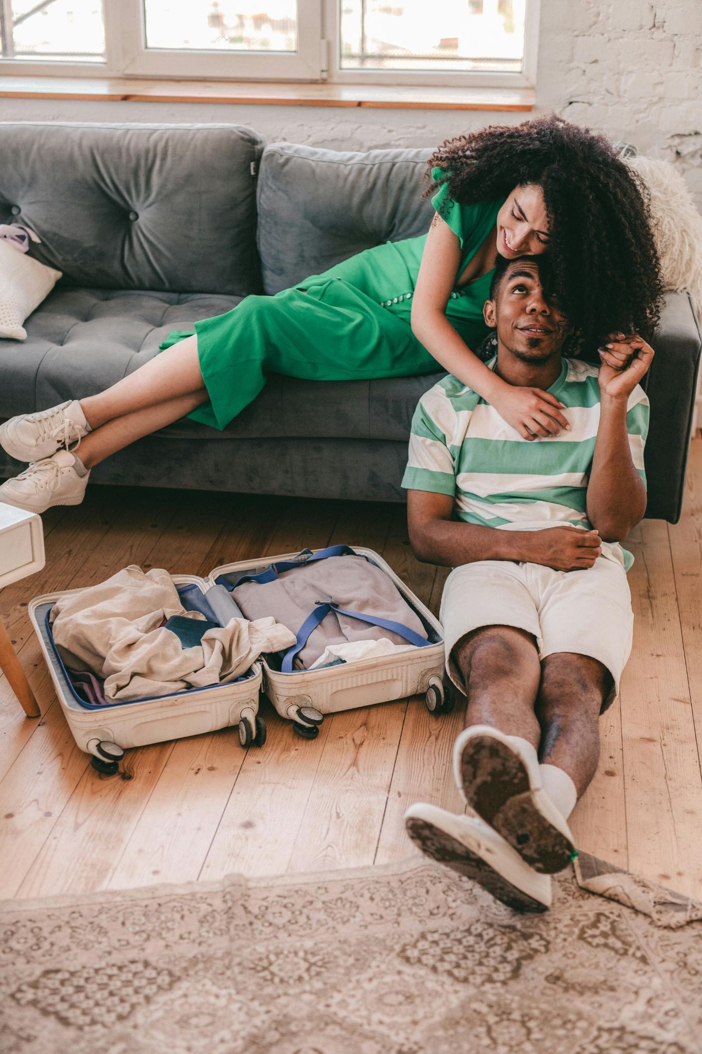 woman lying across sofa, leaning on man sitting on the floor next to an open packed suitcase