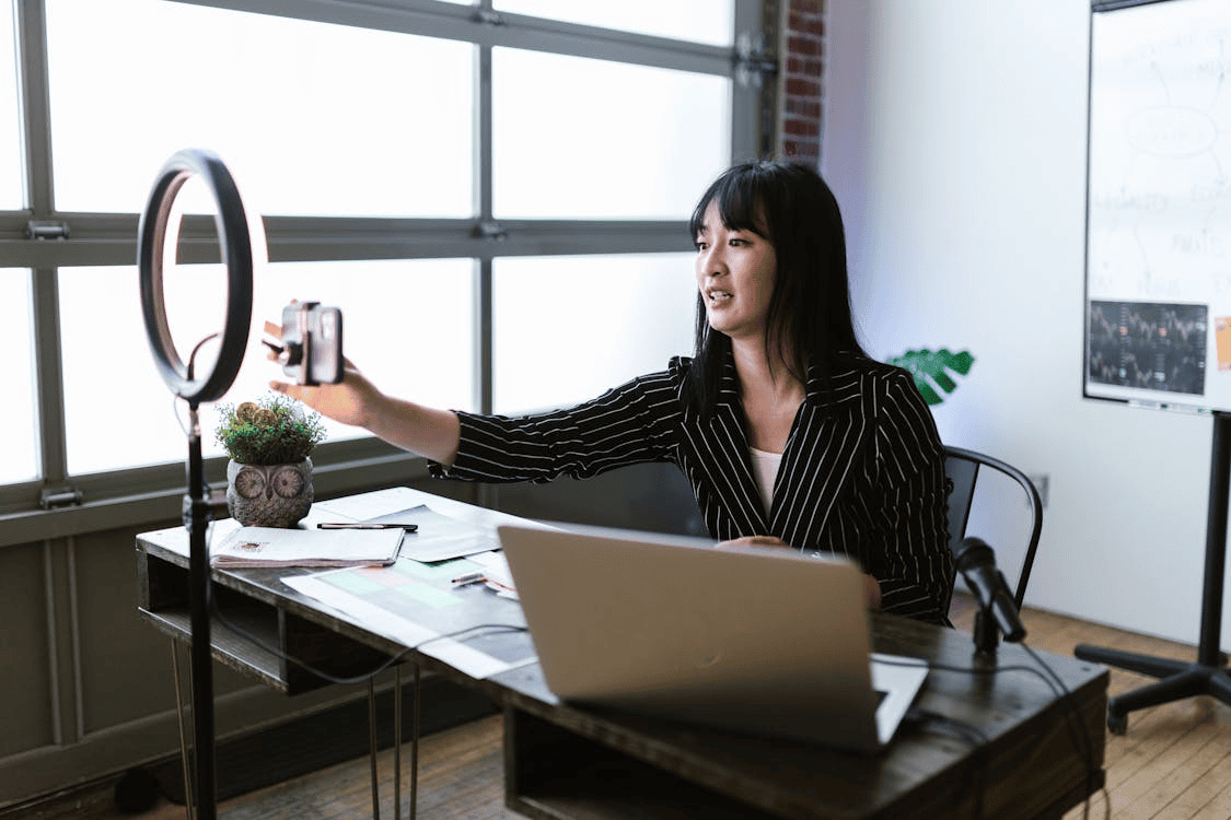 woman sitting at desk with phone attached to ring light