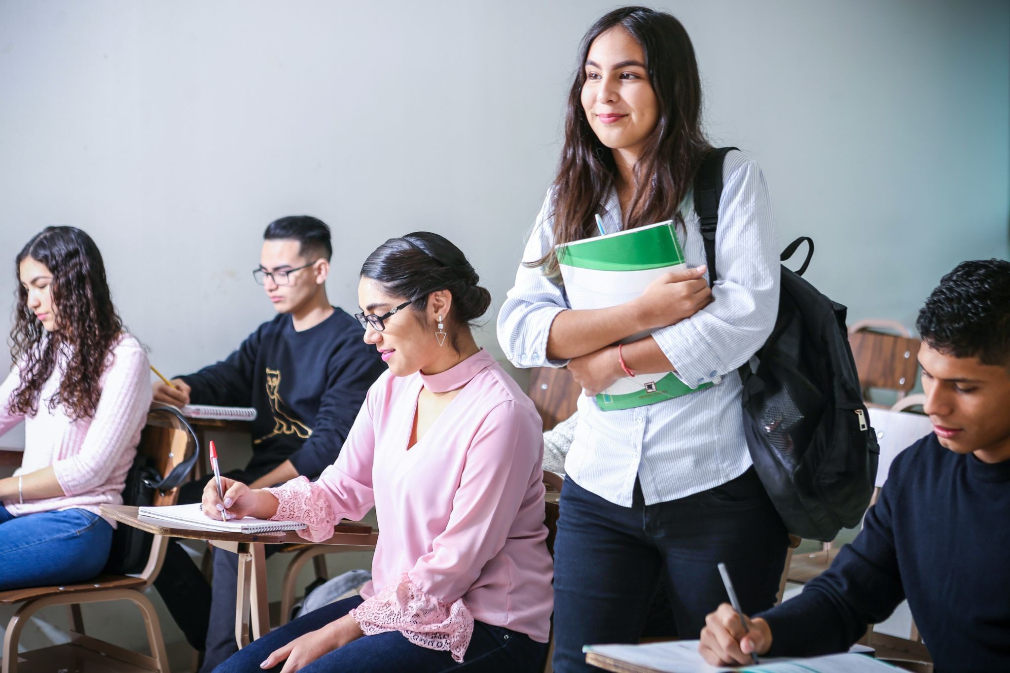 students sitting at desks with one woman standing near them holding books and smiling