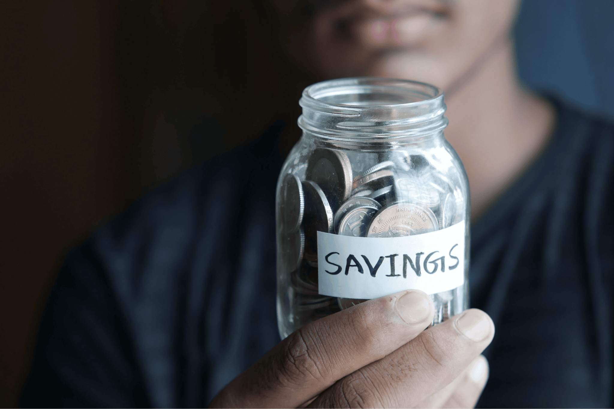 person holding glass jar full of coins with a label saying 'savings'
